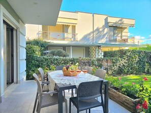 Un patio al aire libre con una mesa dispuesta para dos, rodeado de sillas y un pequeño jardín con plantas y flores.