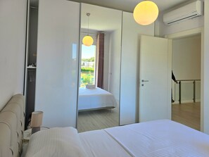 Quarto de hotel com cama, mesa de cabeceira, luminária, guarda-roupa e vista para o exterior.