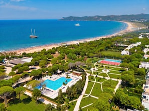 Vista aérea de un complejo turístico frente al mar con piscina, canchas de tenis y playa.