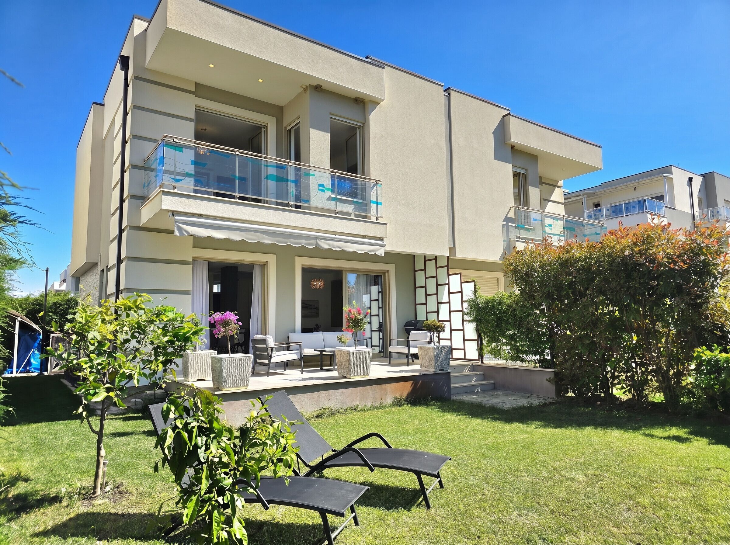 A modern two-story building with a balcony, outdoor seating, and a well-maintained lawn.