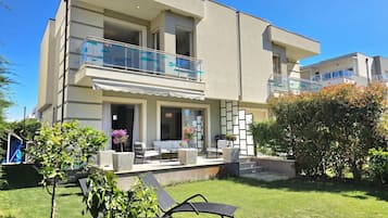 A modern two-story building with a balcony, outdoor seating, and a well-maintained lawn.
