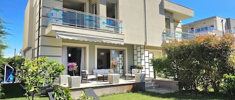 A modern two-story building with a balcony, outdoor seating, and a well-maintained lawn.