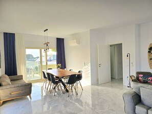 A modern living room with a dining area, a sofa, a coffee table, and a view of the outdoors.