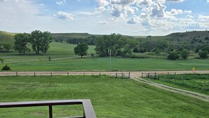 A grassy field with a fence and a road in the distance. - Canyon Acres Ranch • Horse-Friendly Kansas Retreat (Russell)