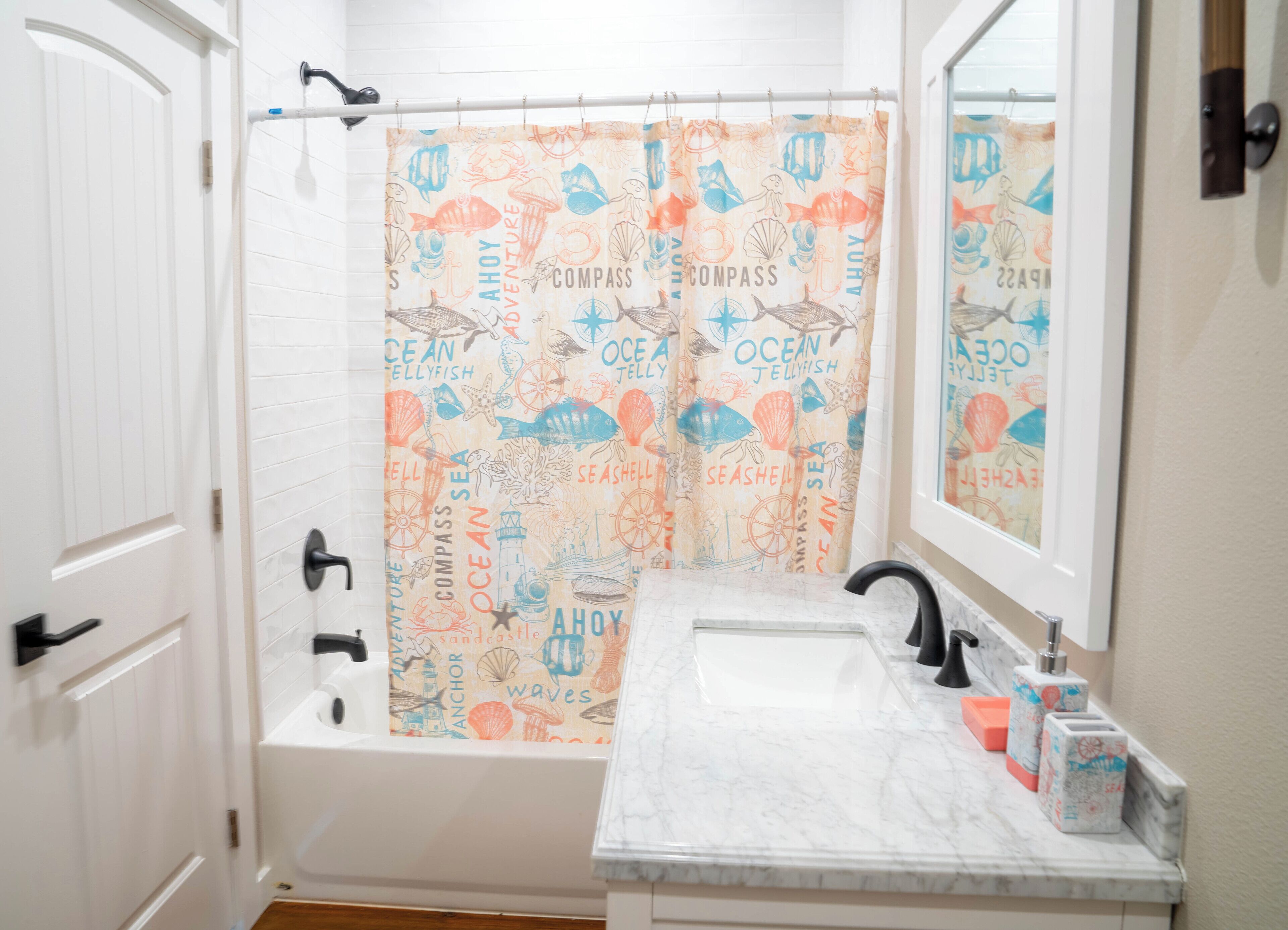 A bathroom with a white bathtub, a sink with a marble countertop, and a shower curtain with ocean-themed designs.