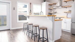 A modern kitchen with a central island, bar stools, and built-in shelves. - Charming 2-bedroom house in Wonderful Bolivar Peninsula with AC, WiFi (Bolivar Peninsula)
