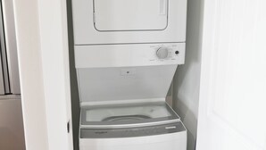 A compact, white laundry room with a front-loading washing machine and dryer. - Charming 2-bedroom house in Wonderful Bolivar Peninsula with AC, WiFi (Bolivar Peninsula)