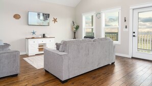 A living room with a gray sofa, a white cabinet, and a wooden floor. - Charming 2-bedroom house in Wonderful Bolivar Peninsula with AC, WiFi (Bolivar Peninsula)
