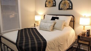 Una cama bien hecha con un plaid blanco y negro a rayas, dos lámparas de pared y dos obras de arte colgadas sobre la cama.