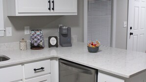 Una cocina con armarios blancos, una cafetera, un escurreplatos y un refrigerador.