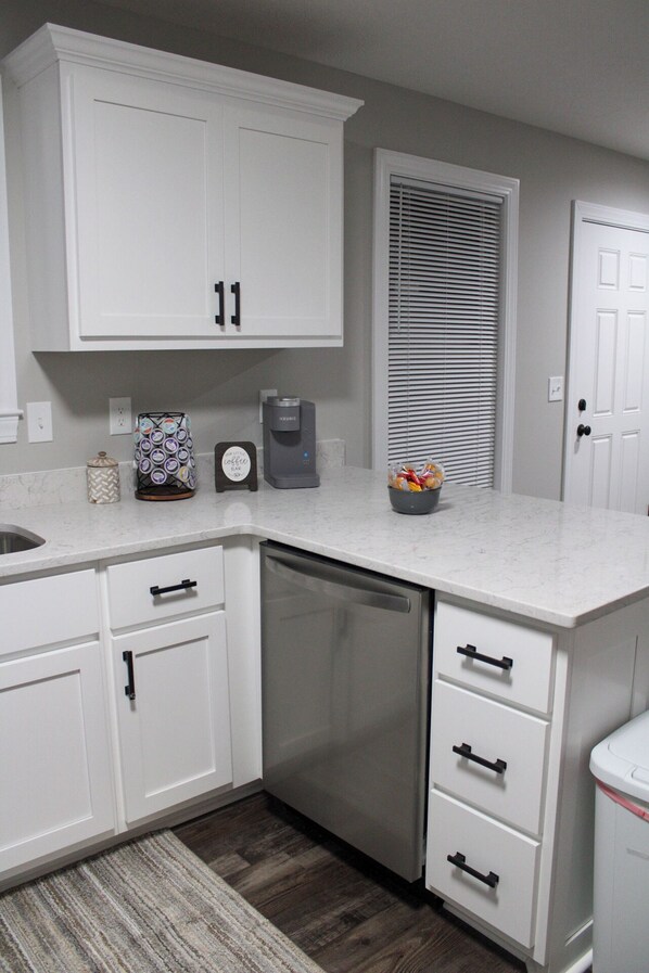 A kitchen with white cabinets, a coffee maker, a dish rack, and a refrigerator. - Hidden Gem #2 (Savannah)
