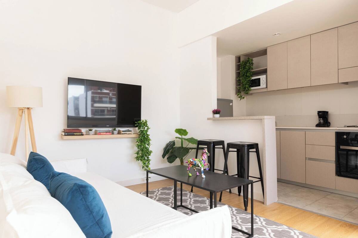 Una sala de estar moderna con televisor de pantalla plana, sofá, mesa de centro y un pequeño comedor.