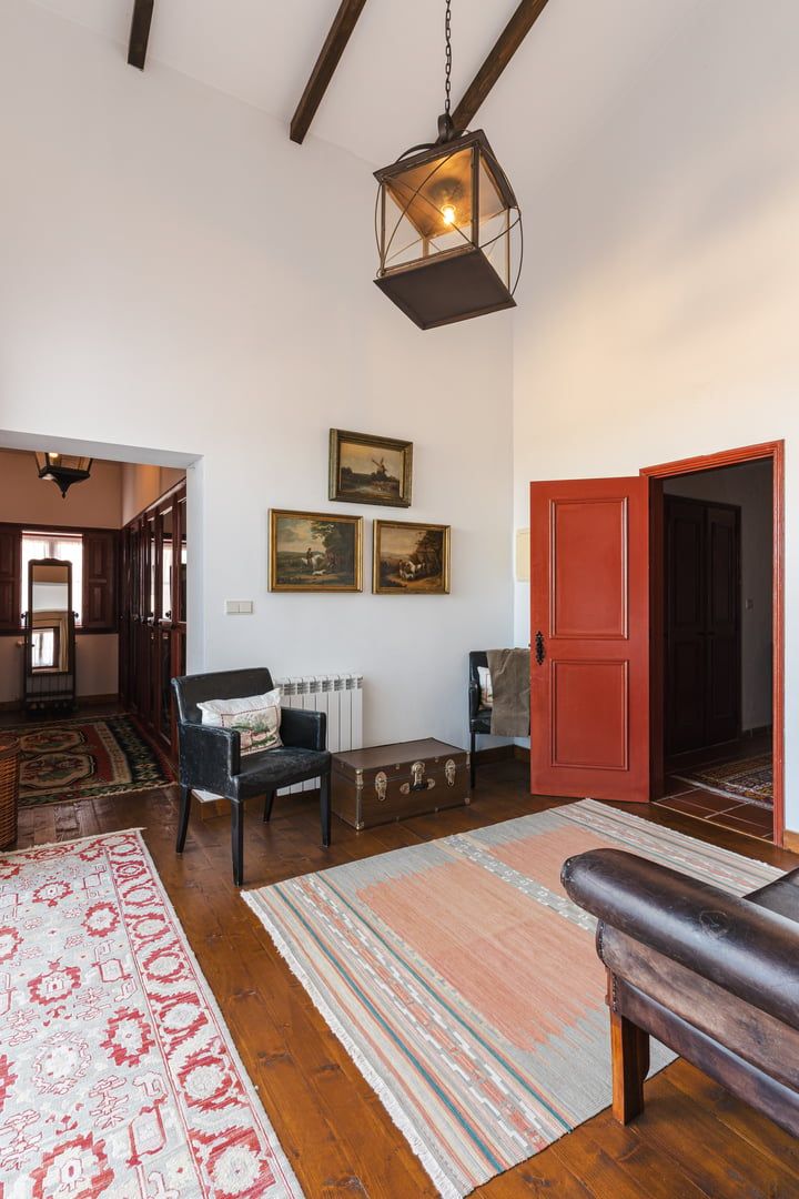 Un salón amplio con suelo de madera, un banco, una puerta roja y un farol colgante.