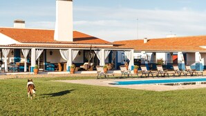 A building with a tiled roof, a covered patio with chairs and tables, and a swimming pool. - Charming Farm House With Pool (Ferreira do Alentejo)