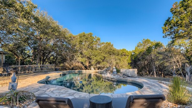 Une piscine bordée de pierres, entourée d’arbres et dotée d’un patio aménagé avec du mobilier d’extérieur.