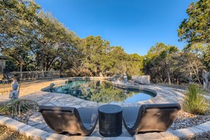 Une piscine bordée de pierres, entourée d’arbres et dotée d’un patio aménagé avec du mobilier d’extérieur.