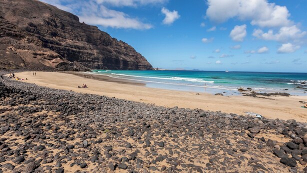 Ein Strand mit felsigem Vordergrund, blauem Himmel und ruhiger See.