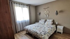 Un dormitorio con una cama, dos mesitas de noche, una lámpara de pared y una ventana con cortinas.