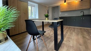 Moderni keittiö, jossa on puiset kaapit, ruokapöytä tuoleineen ja ruukussa oleva kasvi.