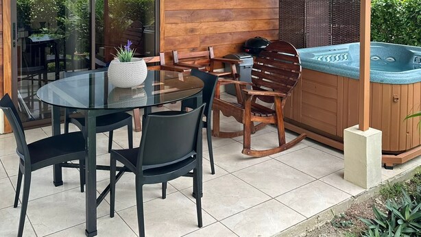 Un patio couvert avec une table en verre, des chaises et un jacuzzi.