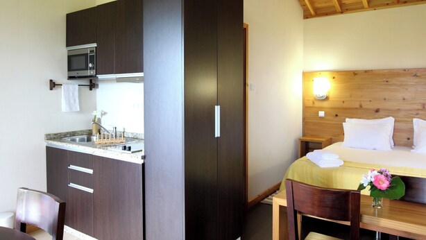 A compact room with a kitchenette, a bed with a wooden headboard, and a small dining area. - Casa Avó Filomena West (Santo Amaro)