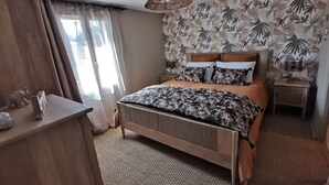 Un dormitorio con cama, mesita de noche, lámpara y ventana con cortinas.