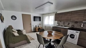 Un espacio habitable compacto con sofá, mesa de comedor, sillas, lavadora y zona de cocina.