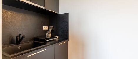 Une cuisine moderne dotée d’un plan de travail noir, d’un évier en acier inoxydable et d’un four encastré.