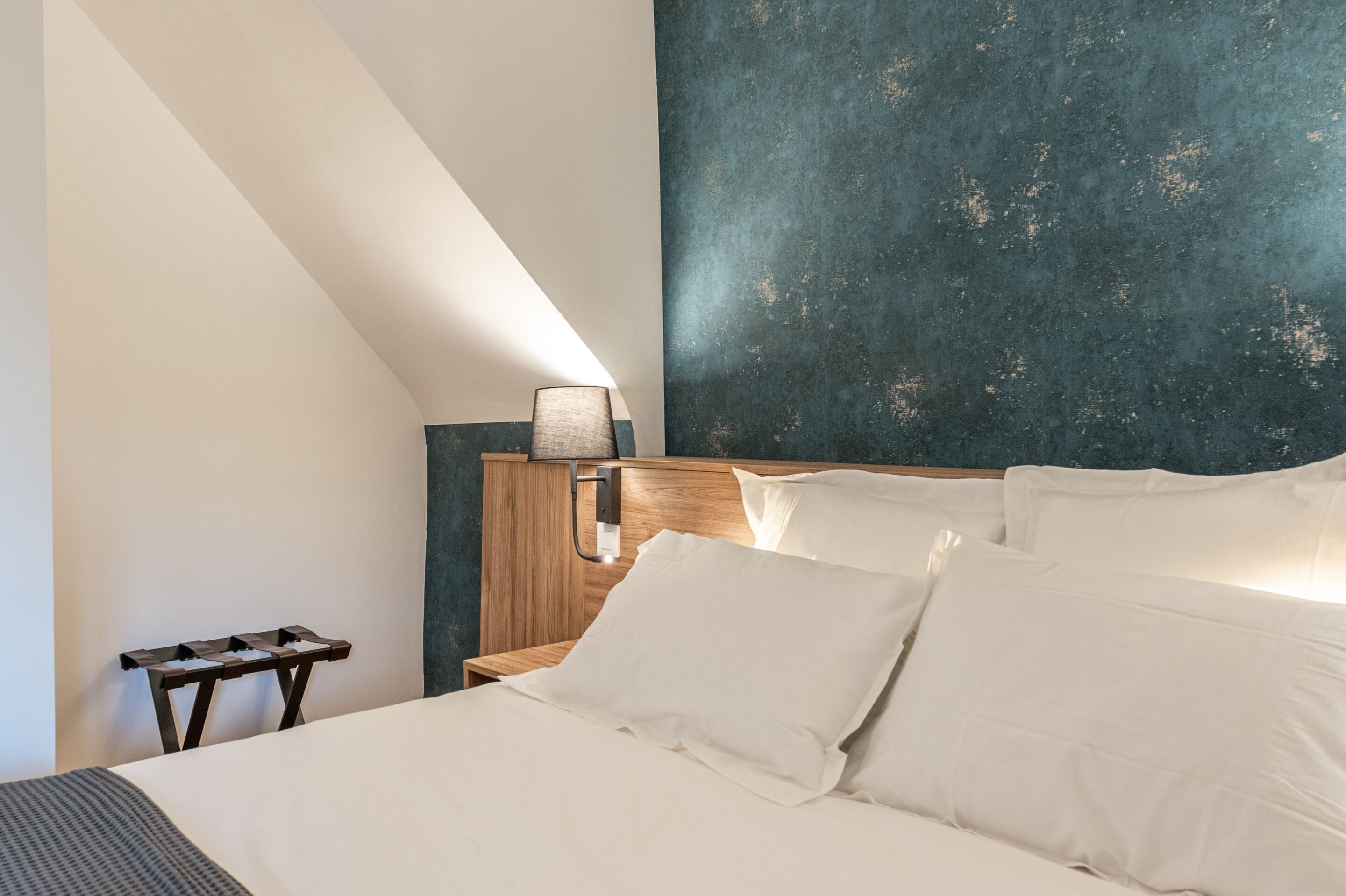 A bedroom with a sloped ceiling, a wooden headboard, white bedding, and a small bedside table.