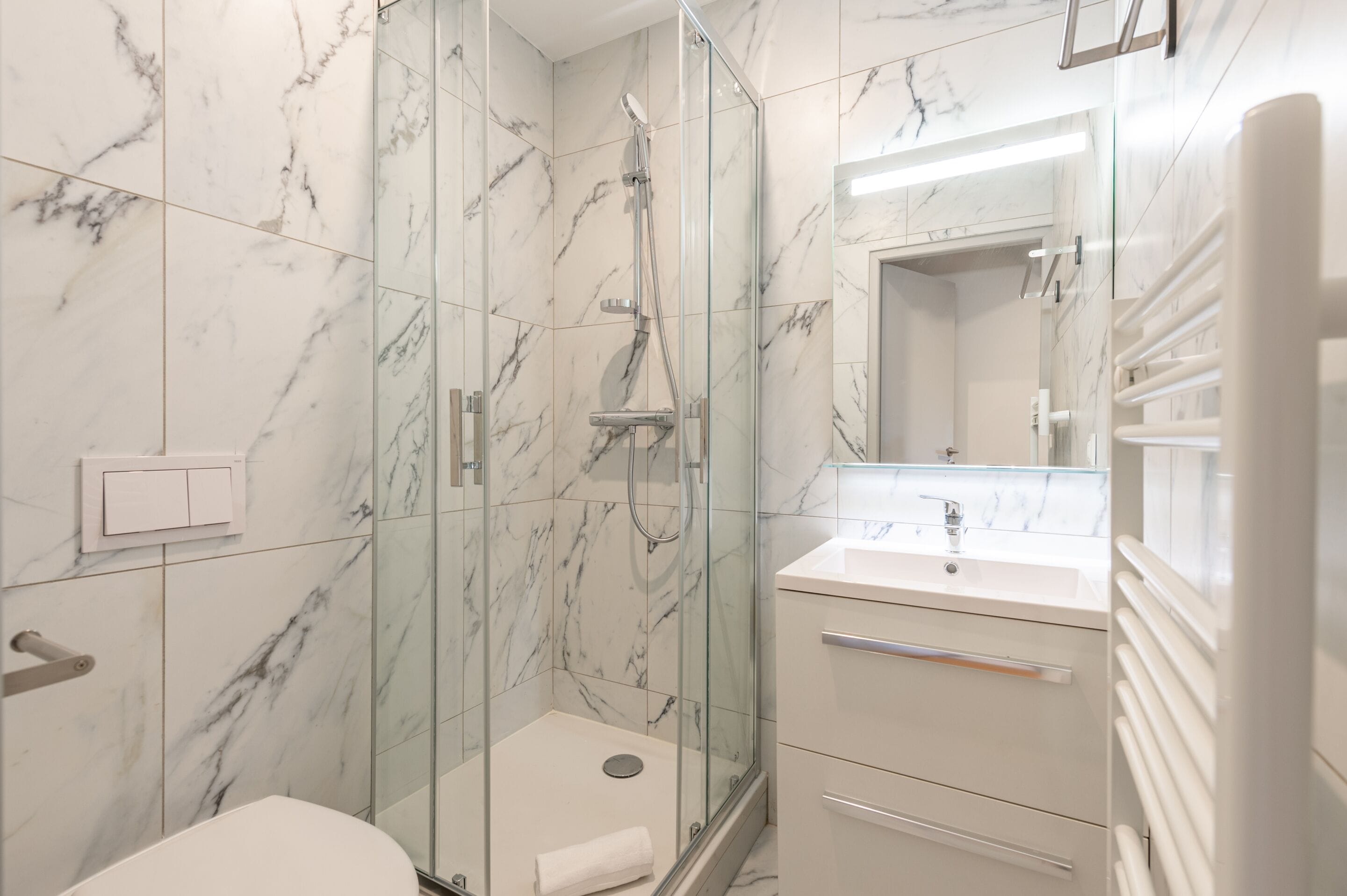 A modern bathroom with a glass-enclosed shower, a white sink, and marble-tiled walls.