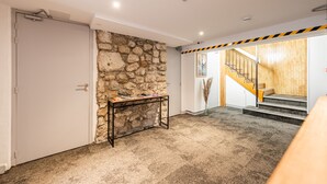 A hallway with a stone wall, a closed door, a small table with books, and a staircase with wooden steps. - Les Tonnelles (Sevrier)