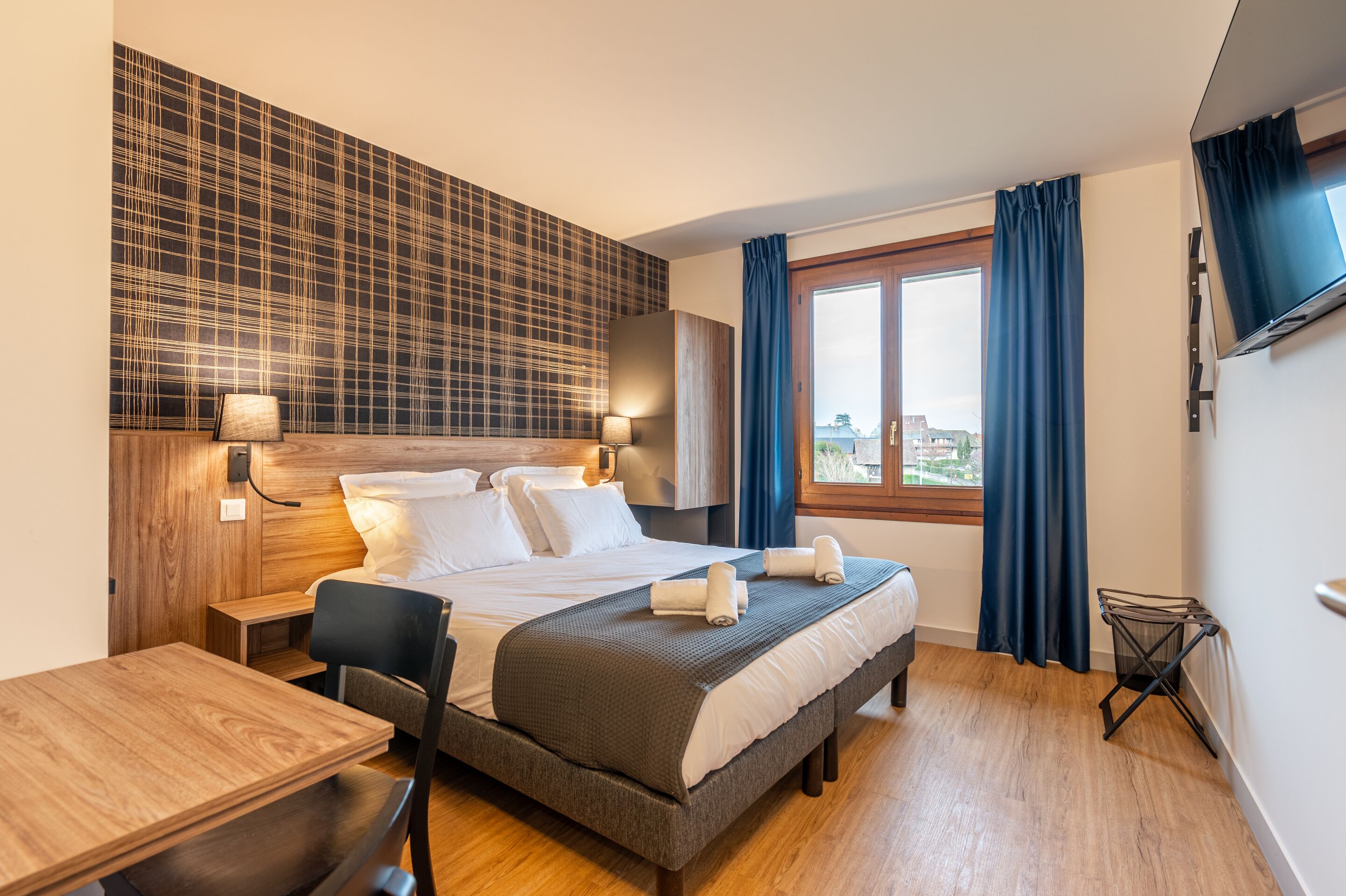 Una habitación de hotel moderna con una cama grande, un escritorio de madera y vistas a la ciudad por la ventana.
