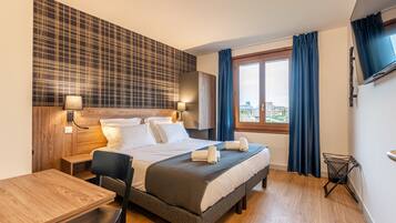 Una habitación de hotel moderna con una cama grande, un escritorio de madera y vistas a la ciudad por la ventana.