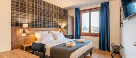 Una habitación de hotel moderna con una cama grande, un escritorio de madera y vistas a la ciudad por la ventana.