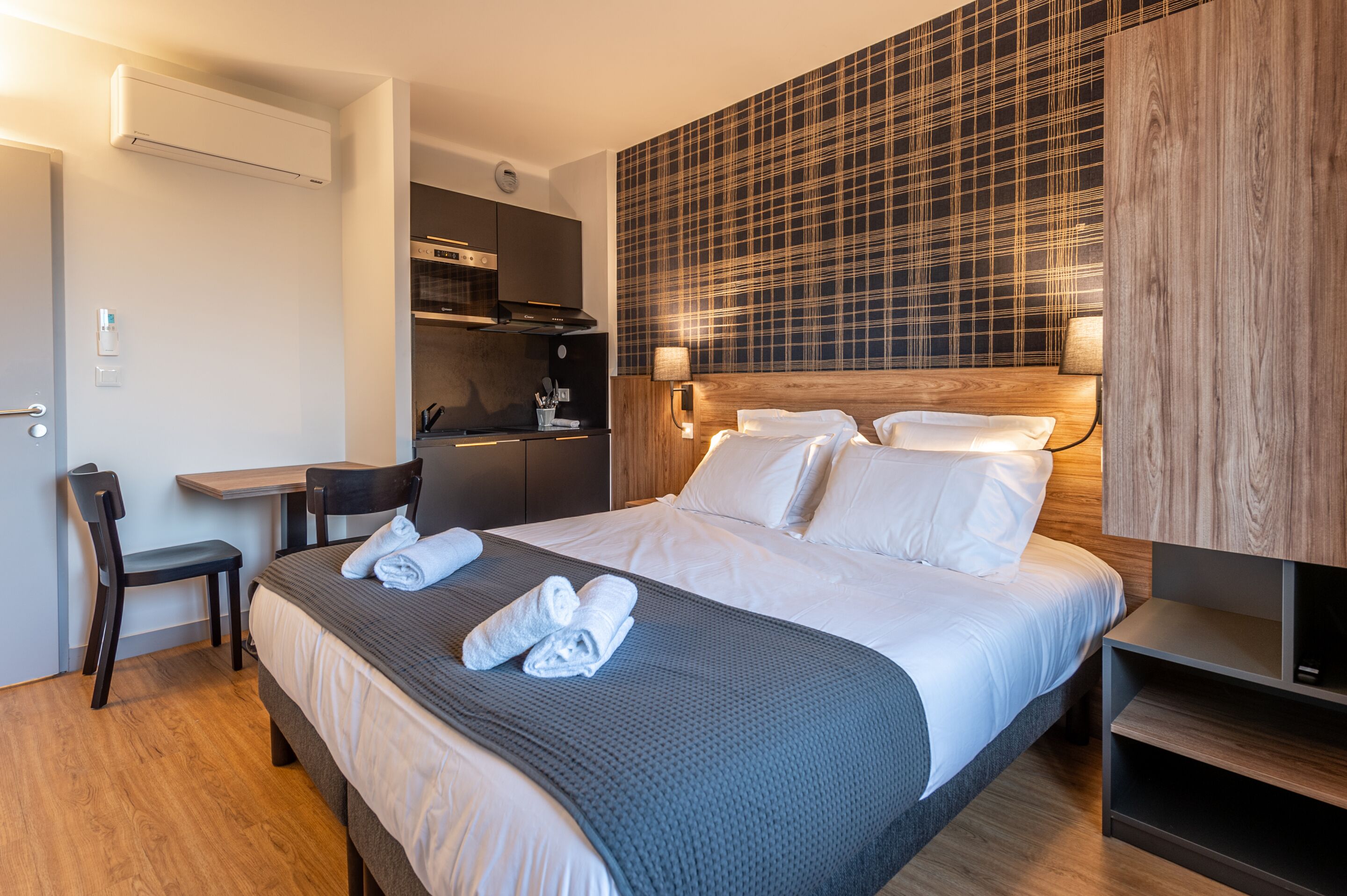 A hotel room with a bed, a desk, a chair, and a kitchenette.