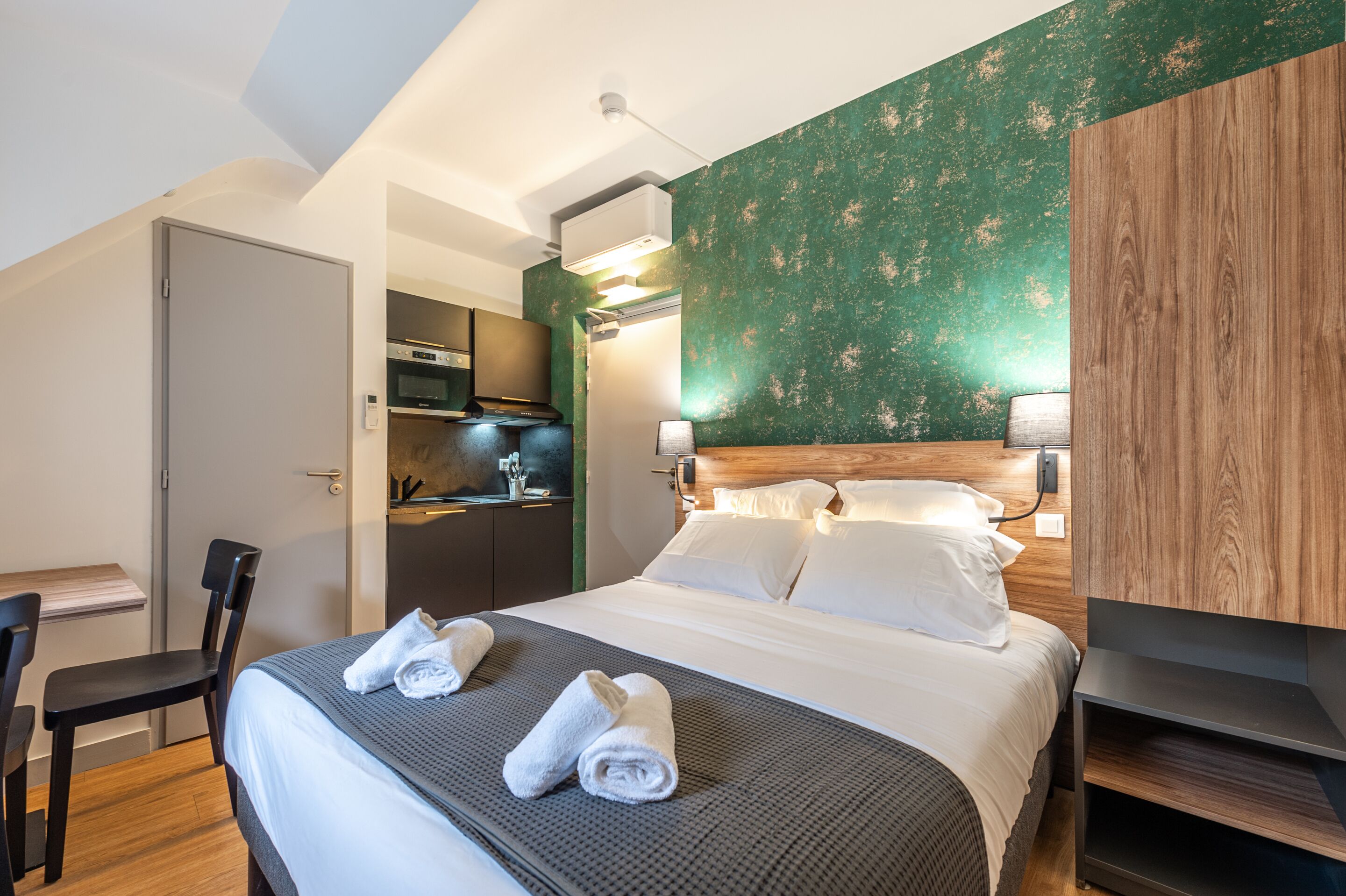 A hotel room with a bed, a desk, and a kitchenette.
