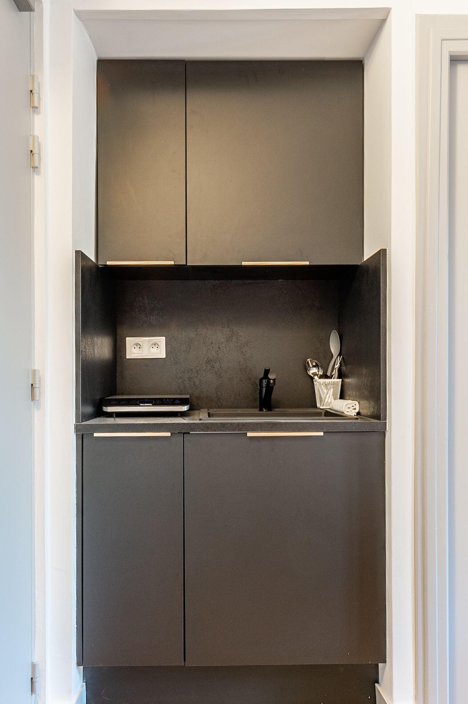 Una cocina moderna con armarios oscuros, horno empotrado y una encimera con hervidor y utensilios.