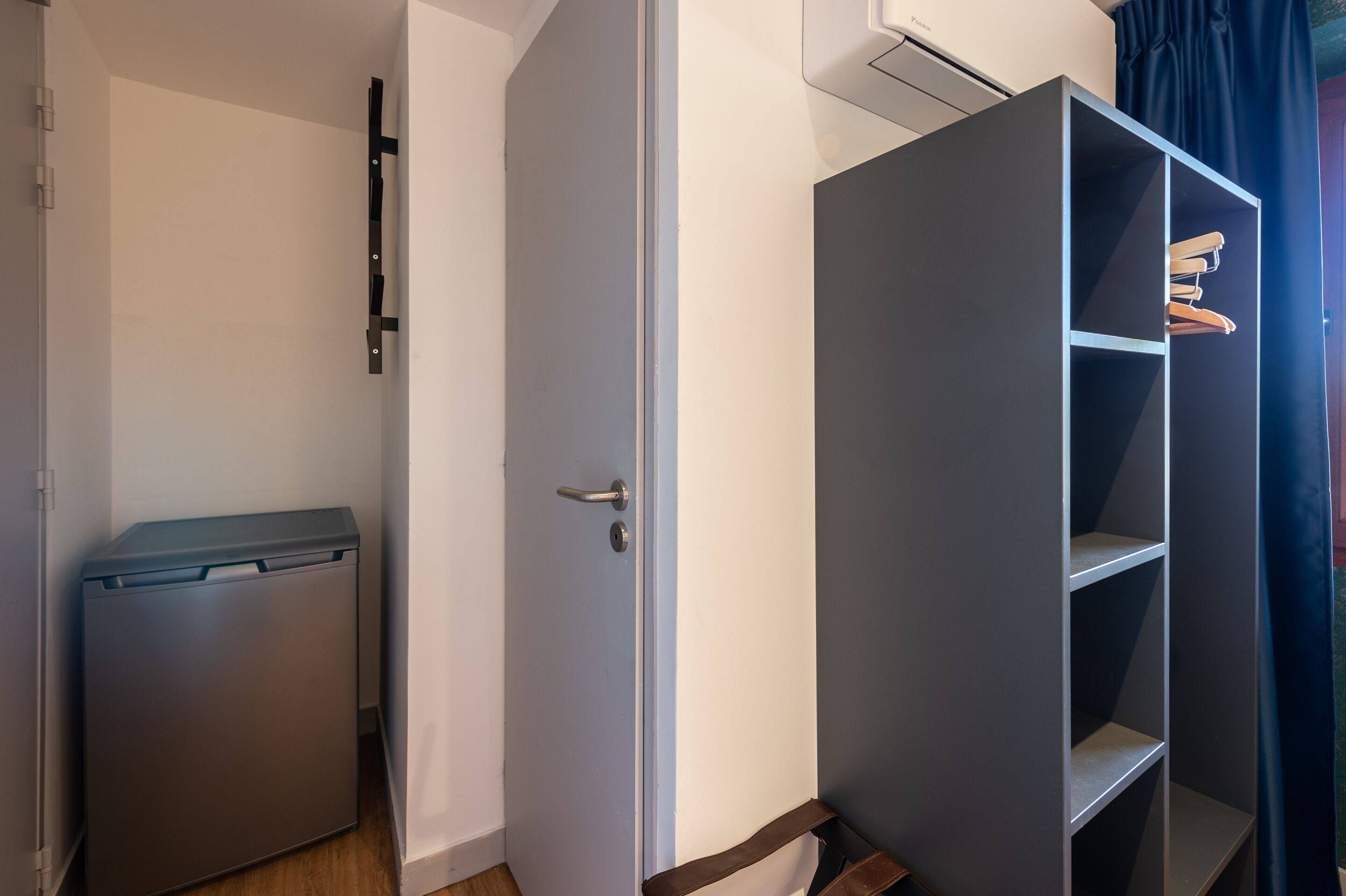 A room with a closed door, a small storage unit, and a wardrobe with shelves.