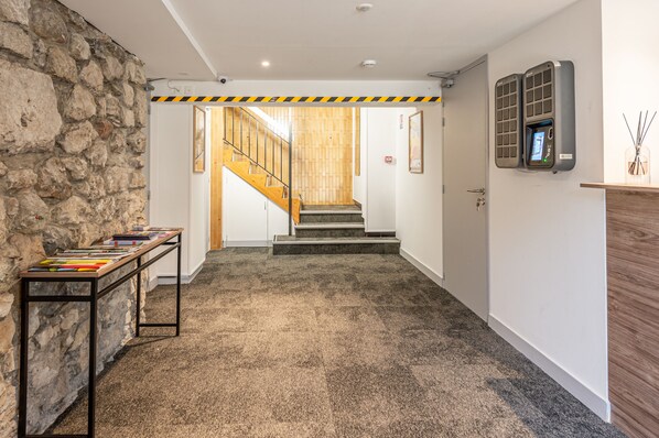 A hotel lobby with a stone wall, a wooden staircase, a reception desk, and a digital display on the wall. - Les Tonnelles (Sevrier)