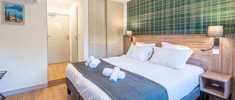 A hotel room with a large bed, a wooden headboard, a nightstand with a lamp, and a green plaid wallpaper.