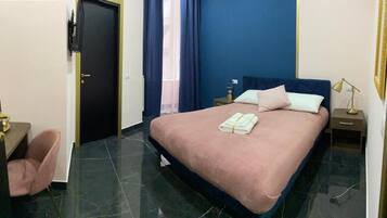 Een hotelkamer met een bed, nachtkastje, stoel, deur en raam met gordijnen.