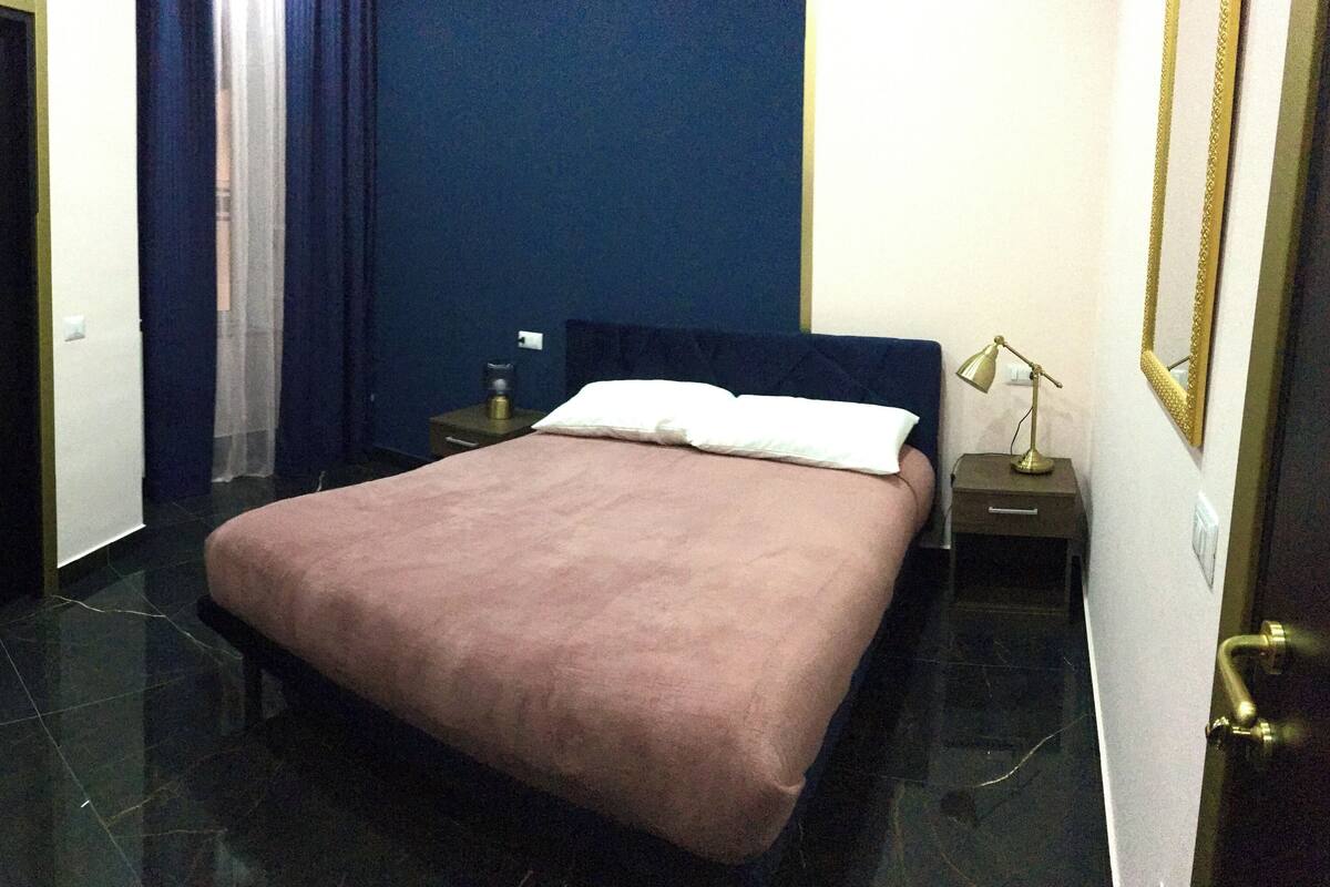 A hotel room with a bed, a nightstand, a lamp, and a door.