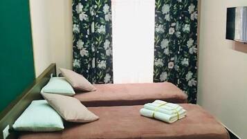 A room with two beds, a desk, a potted plant, and an air conditioning unit.