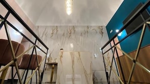 Un intérieur moderne avec un mur en marbre, un escalier doté de rampes en verre et un luminaire suspendu.