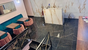 Un intérieur moderne avec un canapé turquoise, des fauteuils roses, un comptoir d’accueil en marbre et un sol en marbre noir.