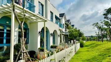 A row of modern houses with balconies, white picket fences, and lush green lawns.