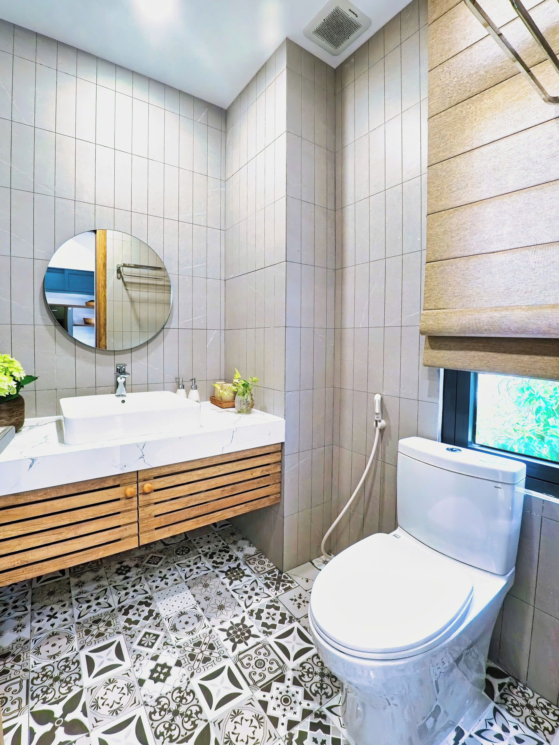 Een moderne badkamer met een wit wastafel, houten wastafelmeubel, een ronde spiegel en een toilet.