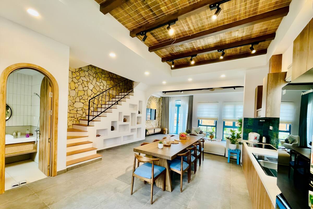 A spacious kitchen with a large island, wooden staircase, and a stone accent wall.