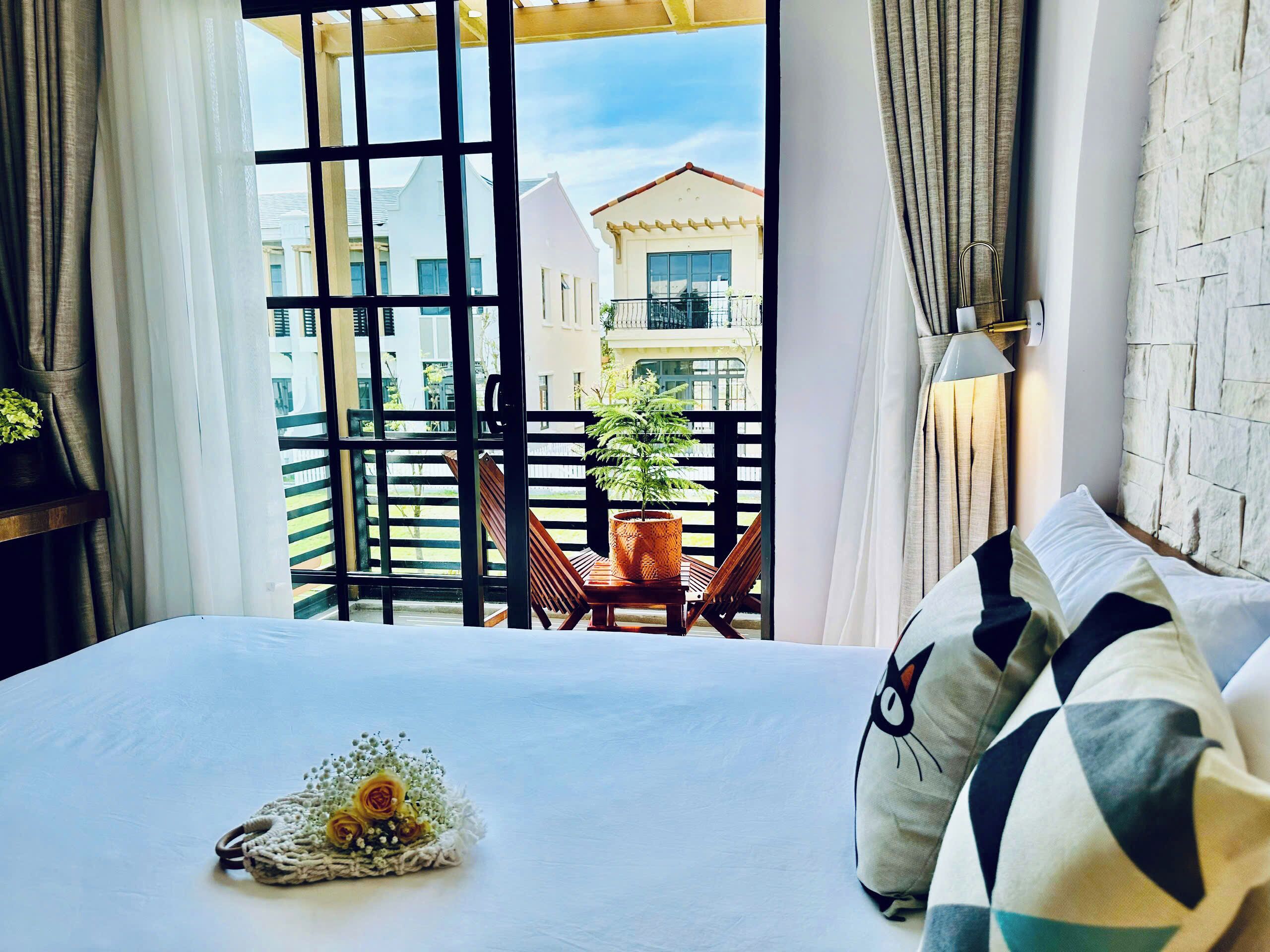 A hotel room with a large bed, a view of the balcony, and a potted plant on the balcony.