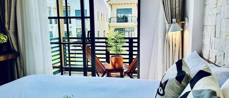 Una camera d'albergo con un grande letto, vista sul balcone e una pianta in vaso sul balcone.